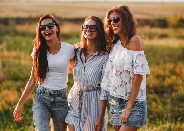 Tre bellissime giovani donne in occhiali da sole in piedi nel campo e sorridente in una giornata di sole . — Foto Stock