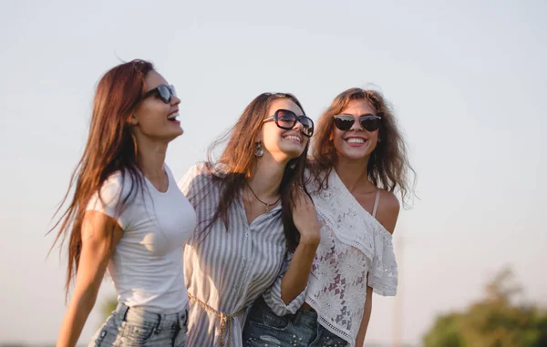 Tre splendide giovani donne in occhiali da sole vestite con i bei vestiti stanno ridendo all'aperto in una giornata di sole . — Foto Stock