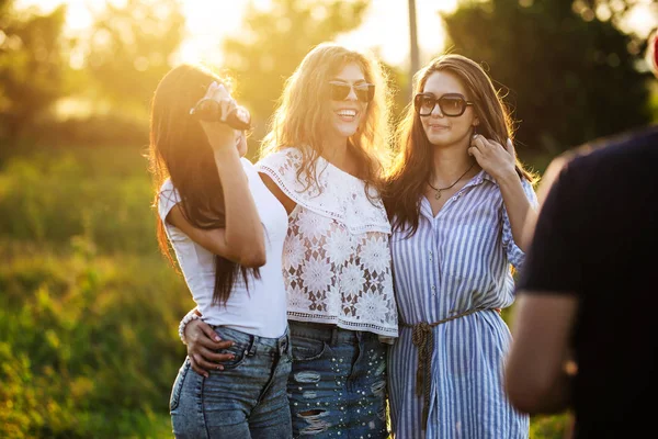 Tre splendide giovani donne dai capelli scuri in occhiali da sole vestite con i bellissimi vestiti stanno posando all'aperto in una giornata di sole . — Foto Stock