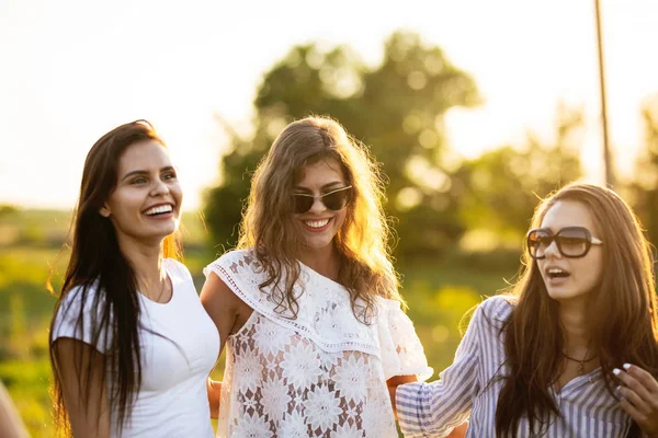 Tre belle giovani donne dai capelli scuri con gli occhiali da sole vestiti con i bei vestiti sorridono e camminano all'aperto in una giornata di sole . — Foto Stock