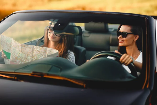 Deux jeunes femmes aux cheveux bruns sont assises dans un cabriolet noir par une journée ensoleillée. L'un d'eux garde la carte entre ses mains. . — Photo