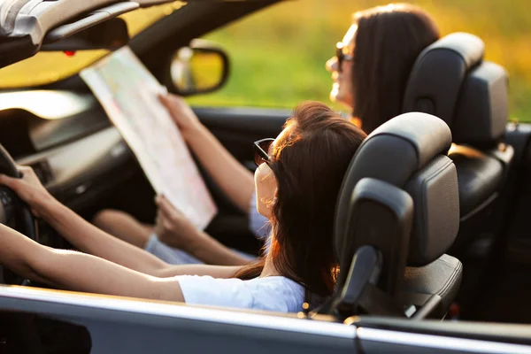 Deux jeunes femmes brunes portant des lunettes de soleil sont assises dans un cabriolet noir par une journée ensoleillée. L'un d'eux garde la carte entre ses mains. . — Photo
