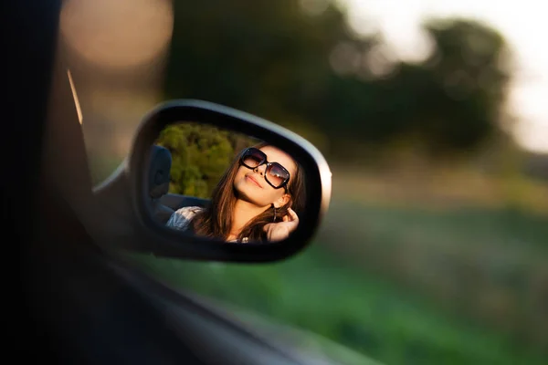 Reflexão de uma linda menina de cabelos escuros em óculos de sol em um espelho lateral de um carro . — Fotografia de Stock