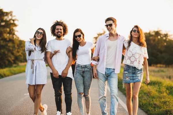 Giovani alla moda due ragazzi e tre ragazze si tengono per mano e camminano sulla strada in una giornata di sole — Foto Stock