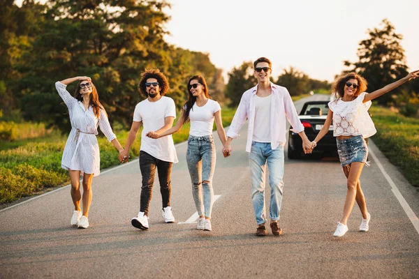 Giovani alla moda due ragazzi e tre ragazze si tengono per mano e camminano sulla strada in una giornata di sole — Foto Stock