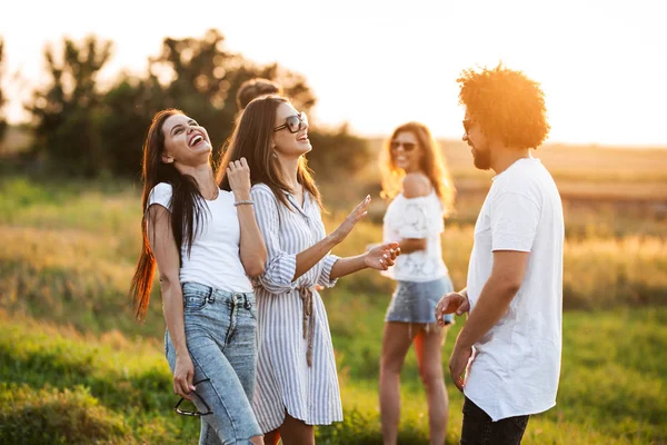 Due giovani donne che chiacchierano e ridono con un giovane uomo riccio all'aperto . — Foto Stock