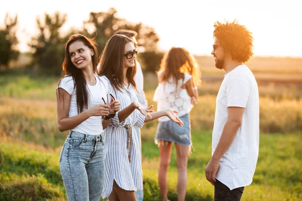 Due giovani donne dai capelli scuri chattano con un giovane uomo riccio all'aperto in una giornata calda . — Foto Stock