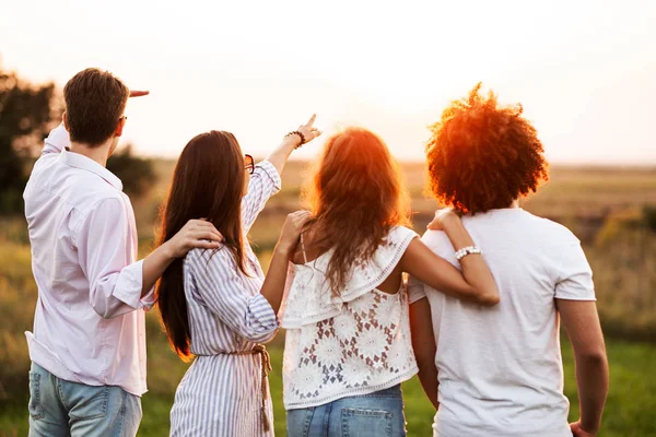 Due giovani ragazzi e due ragazze vestite con abiti eleganti sono in piedi nel campo e guardando di fronte a loro in una giornata di sole . — Foto Stock