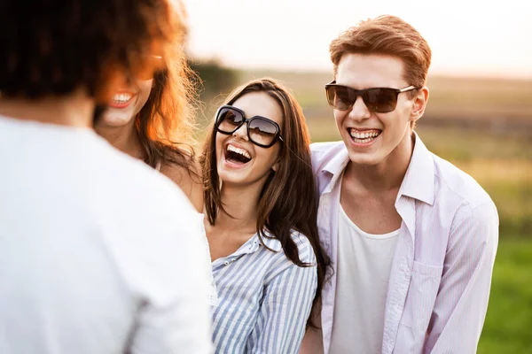 Schöner junger Mann und schöne junge Frau stehen mit Freunden auf dem Feld und lachen. — Stockfoto