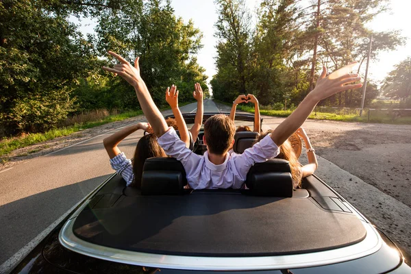 Ompany de jovens andando em um cabriolet na estrada e segurando as mãos para cima em um dia ensolarado quente. Visão traseira . — Fotografia de Stock