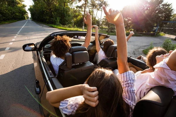 Companhia de jovens montando em um cabriolet na estrada e segurando as mãos para cima em um dia ensolarado quente . — Fotografia de Stock