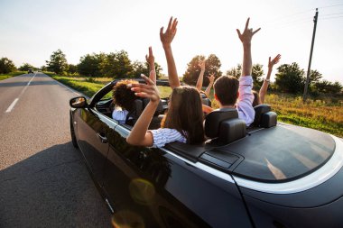 Siyah cabriolet ülke yola çıktı. Genç kızlar ve çocuklar mutlu grup oturuyor araba ambarda ellerini güneşli bir günde.