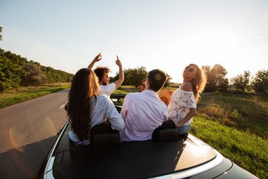 Mutlu genç kızlar ve çocuklar komik şirket güneşli bir günde bir siyah cabriolet yolda oturuyor.