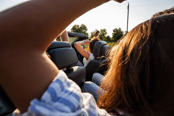 Les jeunes femmes aux cheveux bruns est assis un cabriolet noir avec des amis un jour d'été . — Photo