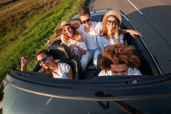 Company of happy young girls and guys are sitting in a black convertible car road on a sunny day. Top view — Stock Photo, Image