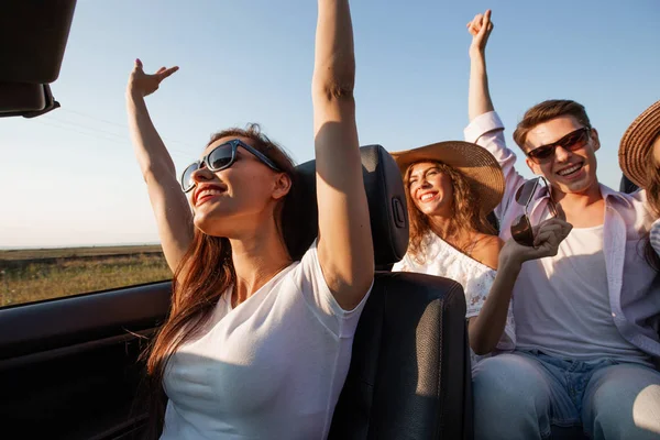 Jovem de cabelos escuros vestida com uma camiseta branca está sentada em um cabriolet preto com amigos em um dia de verão . — Fotografia de Stock