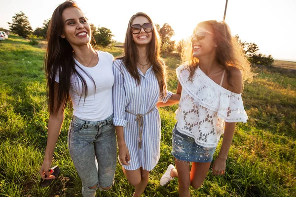 Όμορφες νεαρές γυναίκες σε γυαλιά ηλίου ντυμένος με ωραία ρούχα σταθεί στο πεδίο και χαμογελαστός σε μια ηλιόλουστη ημέρα. — Φωτογραφία Αρχείου