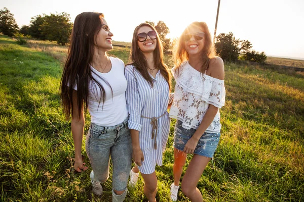 Όμορφες νεαρές γυναίκες σε γυαλιά ηλίου ντυμένος με ωραία ρούχα σταθεί στο πεδίο και χαμογελαστός σε μια ηλιόλουστη ημέρα. — Φωτογραφία Αρχείου
