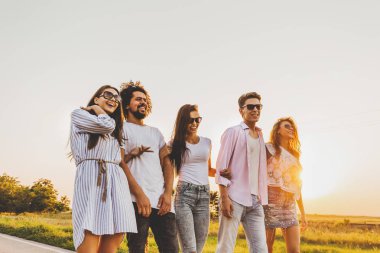 Şık iki genç çocuklar ve üç kız güneşli bir günde bir ülke yolda yürümek