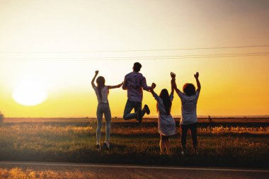 Genç kızlar ve çocuklar Şirket alanında bir yaz gününde atlama ve onların elele. Arkadan görünüm.