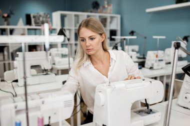 Bir akıllı görünümlü sarışın kadın beyaz gömlek giymiş ile elektrikli dikiş makinesi dikiş var. Moda, terziler atölye.