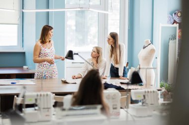 Akıllı görünümlü üç güzel kadınlar dikiş masasında konuşuyor. Terziler aptal arka planda değil. Moda, terziler atölye.