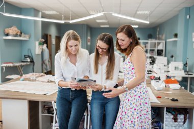 Beyaz gömlek giymiş üç akıllı görünümlü güzel kadınlar dikiş dergide arıyoruz. Moda, terziler atölye.