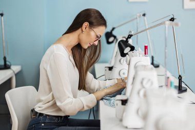 Beyaz gömlek giymiş bir akıllı görünümlü oldukça brunet ile elektrikli dikiş makinesi dikiş kadındır. Moda, terziler atölye.