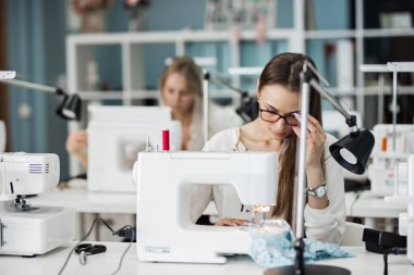 Beyaz gömlek giymiş bir akıllı görünümlü oldukça brunet ile elektrikli dikiş makinesi dikiş kadındır. Moda, terziler atölye.