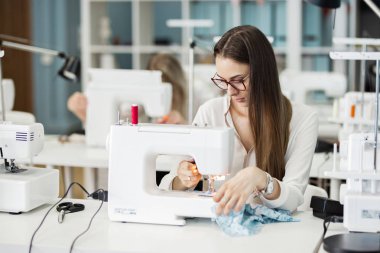 Beyaz gömlek giymiş bir akıllı görünümlü oldukça brunet ile elektrikli dikiş makinesi dikiş kadındır. Moda, terziler atölye.