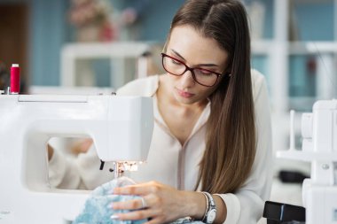 Beyaz gömlek giymiş bir akıllı görünümlü oldukça brunet ile elektrikli dikiş makinesi dikiş kadındır. Moda, terziler atölye.