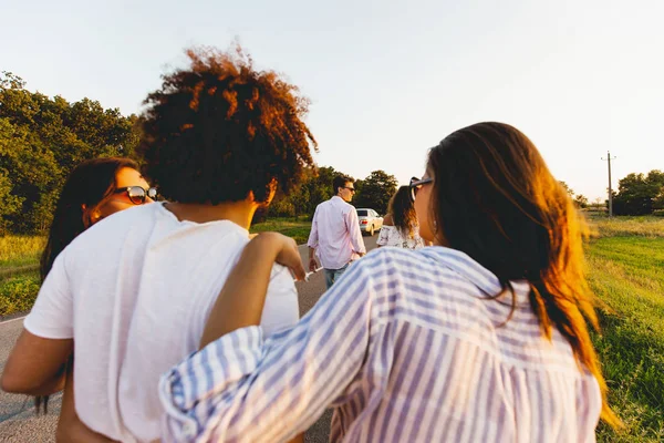 Vista posteriore. giovanotto riccio dai capelli scuri che abbraccia due ragazze. Parlano e camminano lungo la strada . — Foto Stock