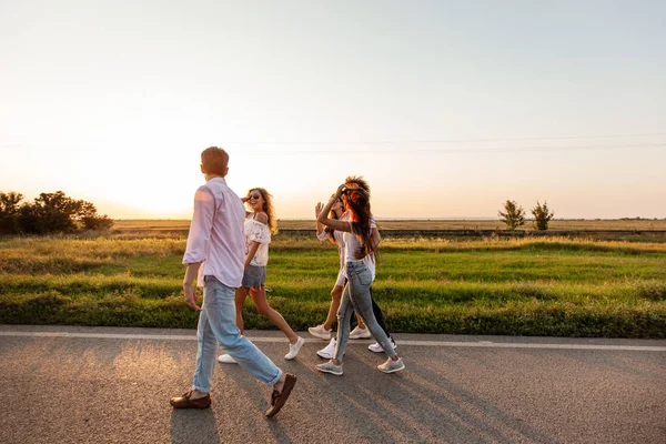 Empresa de jovens felizes e elegantes caminham ao longo da estrada. num dia de sol — Fotografia de Stock