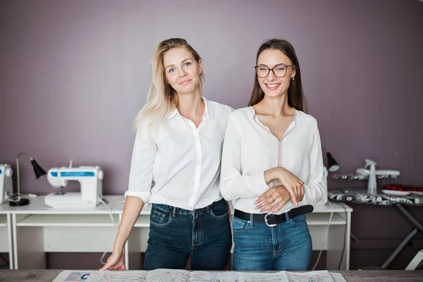Дві розумні красиві жінки в білих сорочках стоять над швейним столом. Мода, майстерня з підйомників . — стокове фото