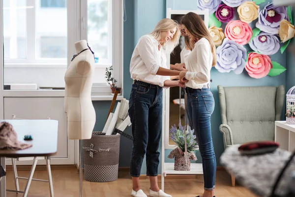 两个穿着白衬衫的漂亮女人站在镜子前互相测量。时尚、裁缝师车间. — 图库照片