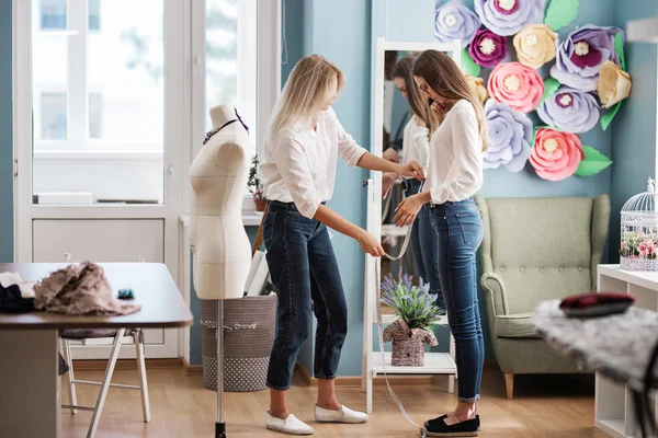 Дві розумні красиві жінки в білих сорочках стоять перед дзеркалом і вимірюють один одного. Мода, майстерня з підйомників . — стокове фото