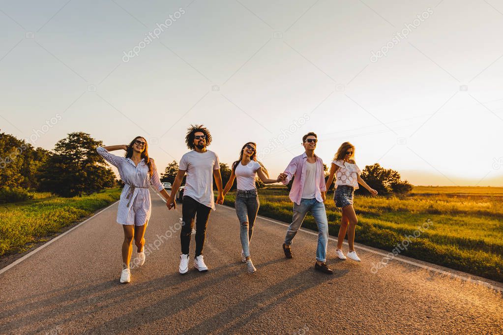 Company of happy young stylish guys walk on a country road on a sunny day