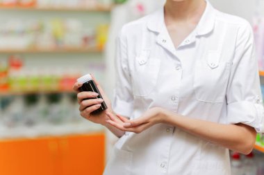 İnce güzel girl.wearing bir laboratuar önlüğü gösterir küçük bir kavanoza kameraya modern bir eczane.