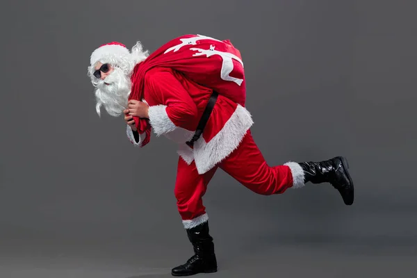 Санта-Клауса з сонцезахисні окуляри працює з мішка в різдвяні подарунки на спині на білому тлі. — стокове фото