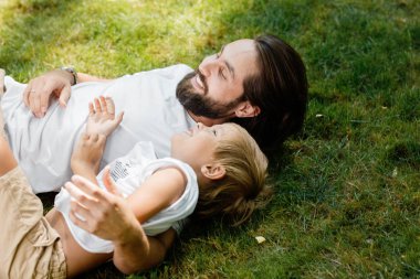 Temiz hava ve gülümsüyor yeşil çim üzerinde küçük çocukla sakallı yakışıklı bir koyu saçlı adam yatıyor.