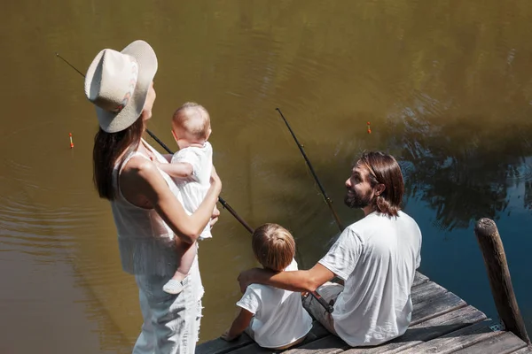Mère avec une petite fille sur les mains regarde comment père et fils pêchent. Toute la famille vêtue de vêtements blancs . — Photo
