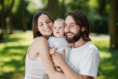 Muhteşem Anne, acımasız baba ve beyaz giysiler giymiş büyüleyici küçük kızları sıcak parkta kucaklayan.