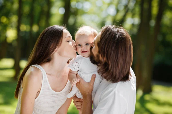 Retrato de uma família feliz. Jovem pai de cabelos escuros e sua bela esposa beijam sua adorável filha bebê — Fotografia de Stock