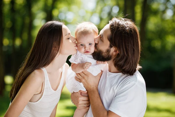 Rodzina romantyczny na świeżym powietrzu. Młoda Ciemnowłosa kobieta i jej mąż są Całowanie ich uroczy córeczkę. — Zdjęcie stockowe