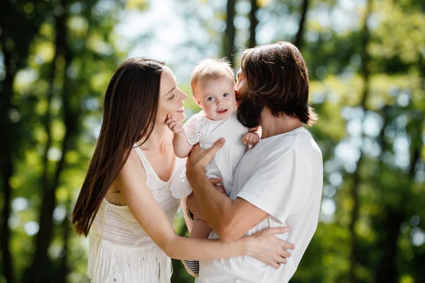 Glückliche schöne Eltern in weißen Freizeitklamotten, die einen sonnigen Tag mit ihrer kleinen Tochter im Park verbringen. — Stockfoto