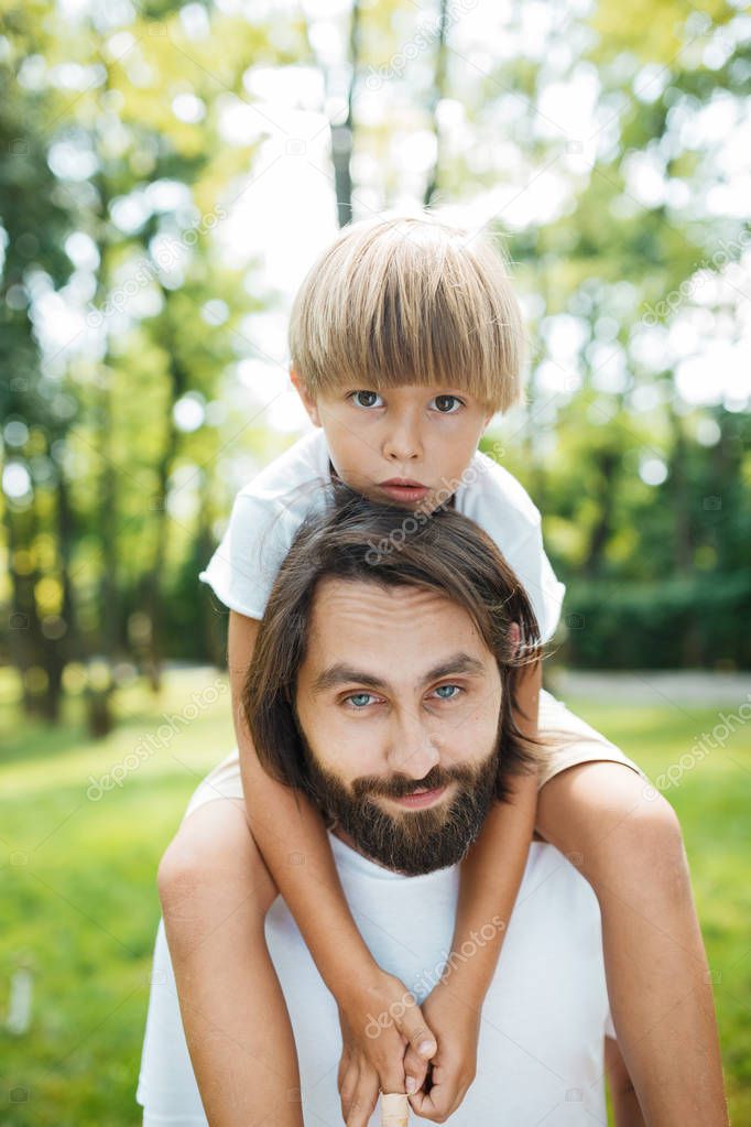 Portrait of a beautiful dark-haired man with blue eyes and a blond boy sitting on his shoulders