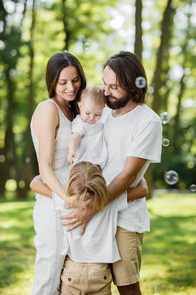 Ehepaar in weißen Kleidern lächelt und hält kleine Tochter in den Armen, während sie Sohn umarmt. — Stockfoto