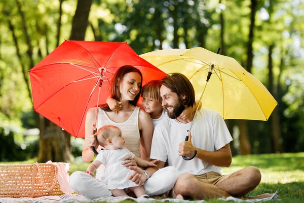 Duże parasole czerwone i żółte, obejmujące ojciec, matka i dzieci ubranych w białe ubrania z jasnym słońcu — Zdjęcie stockowe