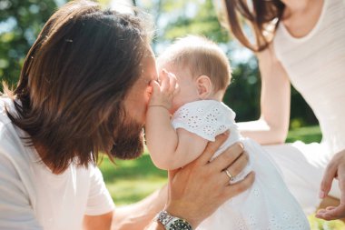 Koyu renk saçlı baba yavaşça kollarında küçük sevimli kızı tutarak ve gözlerinin içine bir yaz günü parkta izlerken..