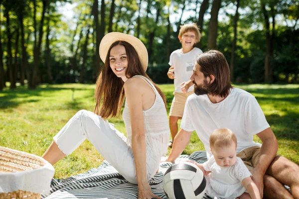 Mère, père, leur fils et leur petite fille, vêtus de vêtements blancs, se reposent sur le pique-nique dans le parc. Famille heureuse . — Photo